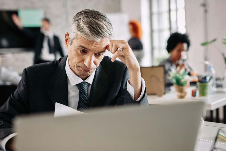A man in a suit intently examines his laptop, showcasing a professional and focused demeanor.