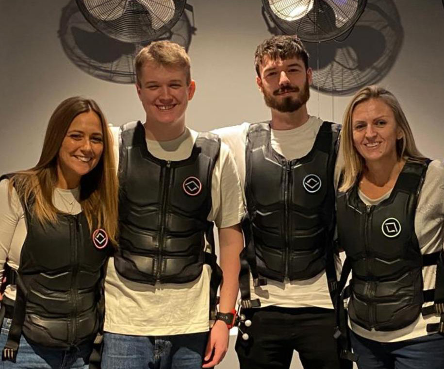 Three individuals in black vests stand, all facing the camera.  