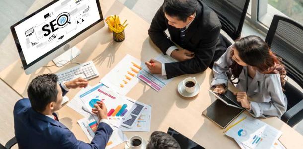 A top-down view of An SEO strategy meeting with four business people and a monitor displaying the word SEO