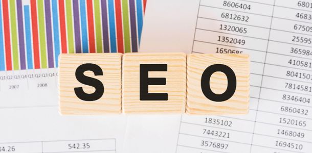 SEO written with wooden blocks with spreadsheets in the background