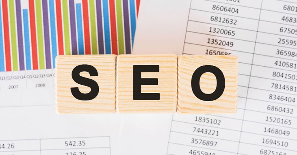 SEO written with wooden blocks with spreadsheets in the background