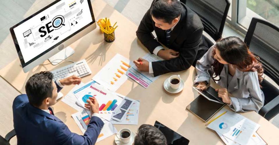 A top-down view of An SEO strategy meeting with four business people and a monitor displaying the word SEO