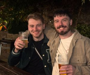 . Two men seated at a table, each holding a beer, engaged in conversation. 