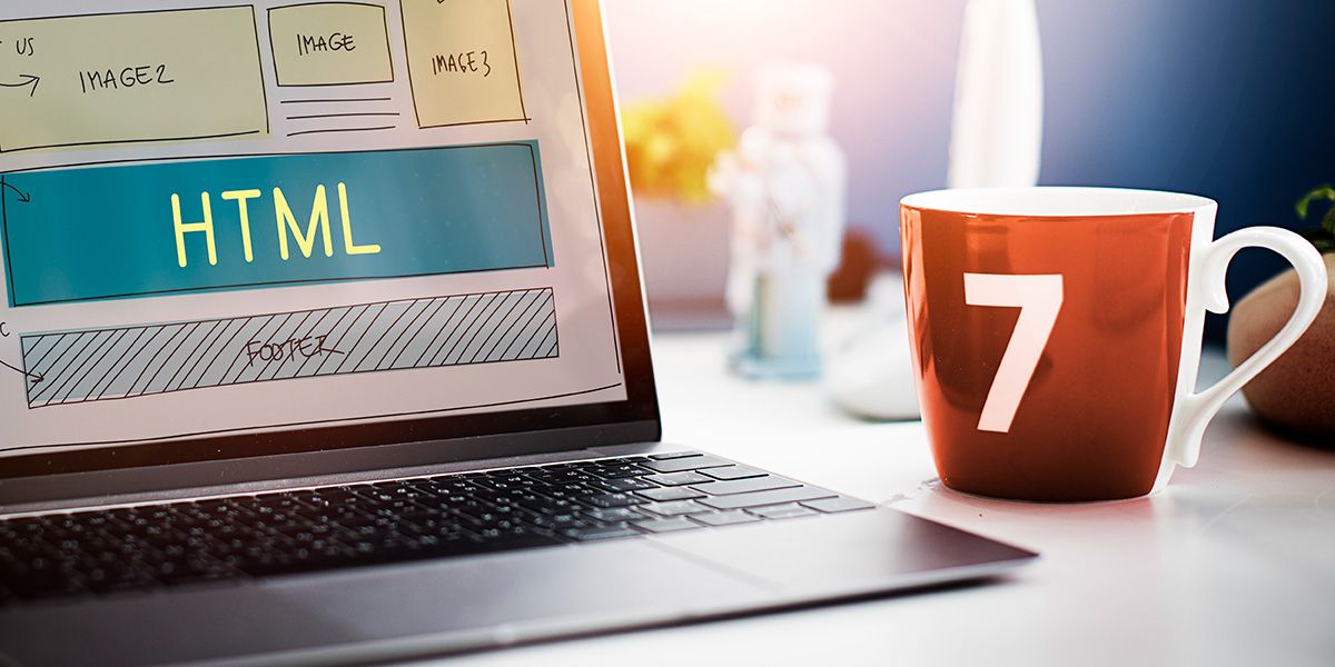 Laptop displaying HTML web design schematics on a desk next to a mug with the number 7 on it