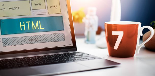 Laptop displaying HTML web design schematics on a desk next to a mug with the number 7 on it