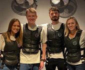 Three individuals in black vests stand, all facing the camera.  