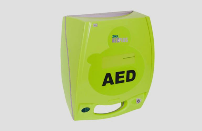 Wall-mounted automated external defibrillator (AED) in a glass case with a red emergency light, labeled for emergency use.