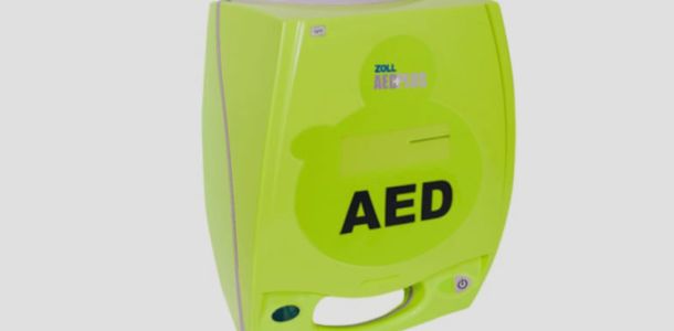 Wall-mounted automated external defibrillator (AED) in a glass case with a red emergency light, labeled for emergency use.