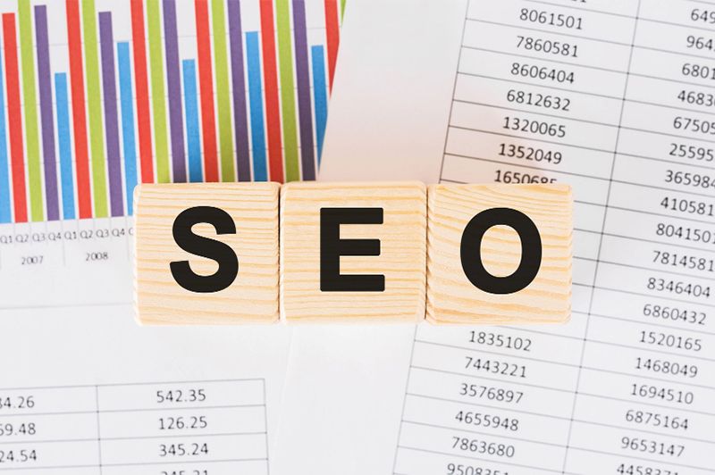 SEO written with wooden blocks with spreadsheets in the background